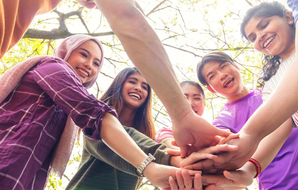 Un equipo diverso de adultos forma un círculo con las manos en la masa.